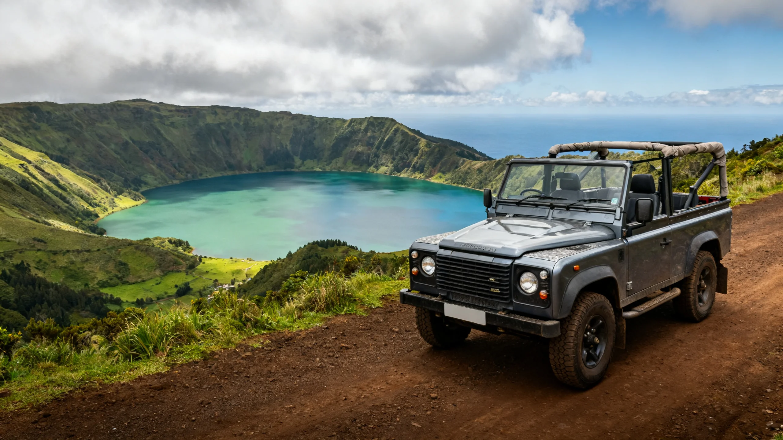 Open-top 4x4 jeep on a dirt road overlooking the Sete Cidades caldera with the green and blue twin lakes visible far below